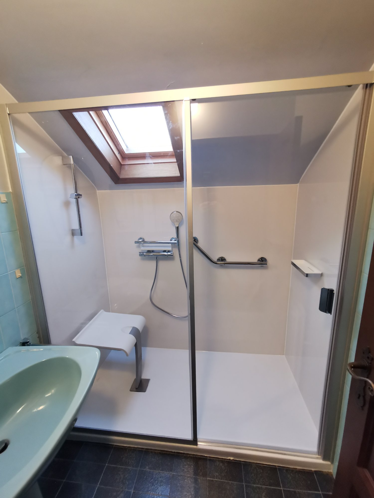 Salle de bain PMR : douche avec receveur extra-plat, siège rabattable et barre d'appui, réalisée par RENOVO