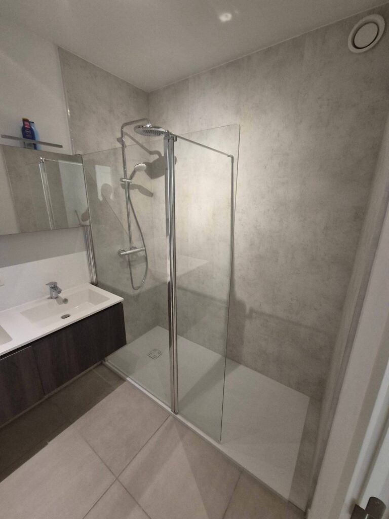 Après : douche walk-in avec panneaux muraux aspect béton clair, receveur extra-plat et colonne de douche thermostatique – RENOVO